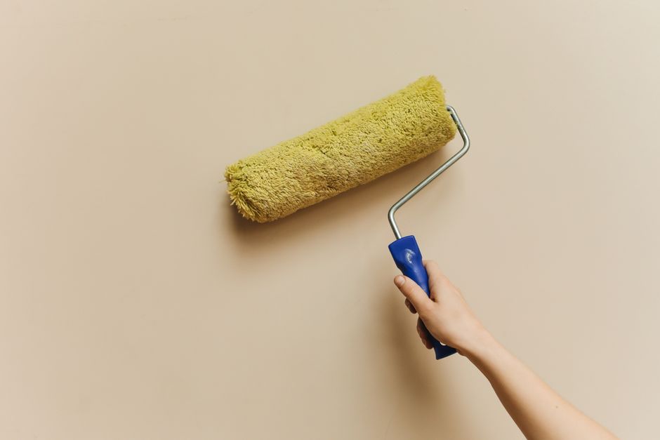 Hand using a paint roller on a beige wall